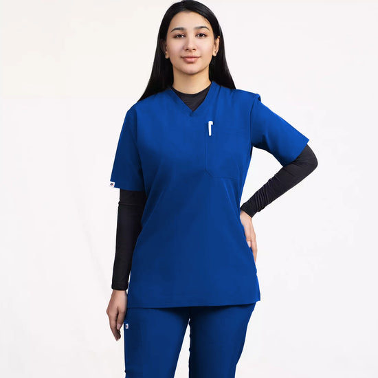 A healthcare professional modeling a matching royal blue V-neck scrub top and pants over a black long-sleeve undershirt against a white studio background.