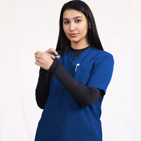 A healthcare professional modeling a royal blue short-sleeve scrub top layered over a black long-sleeve undershirt against a white studio background.
