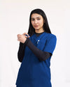 A healthcare professional modeling a royal blue short-sleeve scrub top layered over a black long-sleeve undershirt against a white studio background.