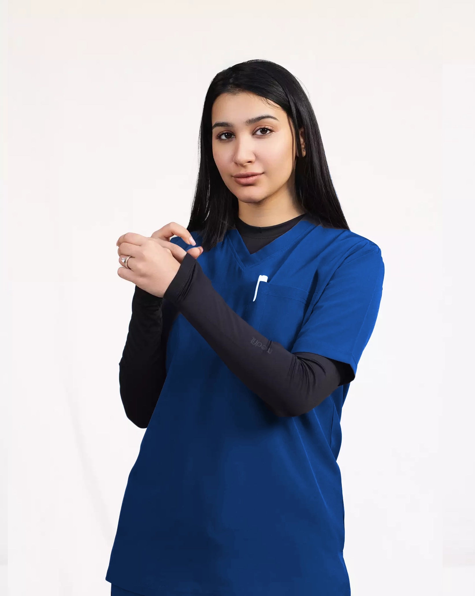 A healthcare professional modeling a royal blue short-sleeve scrub top layered over a black long-sleeve undershirt against a white studio background.