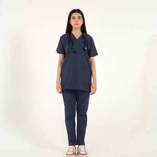 A healthcare professional standing and modeling a matching navy blue medical scrub set, featuring a short-sleeve V-neck top and straight-leg pants with a stethoscope against a white background.