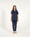 A healthcare professional standing and modeling a matching navy blue medical scrub set, featuring a short-sleeve V-neck top and straight-leg pants with a stethoscope against a white background.