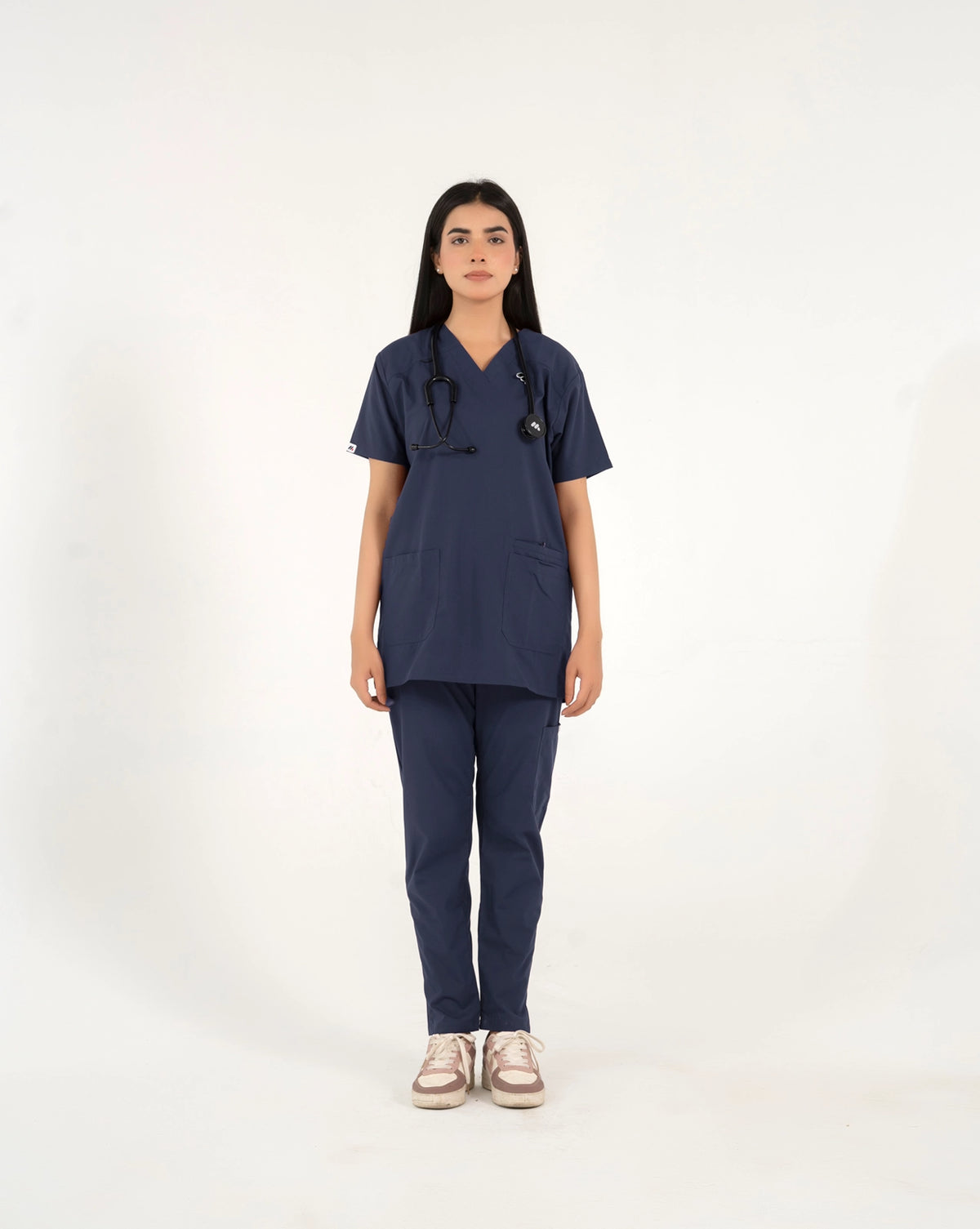 A healthcare professional standing and modeling a matching navy blue medical scrub set, featuring a short-sleeve V-neck top and straight-leg pants with a stethoscope against a white background.